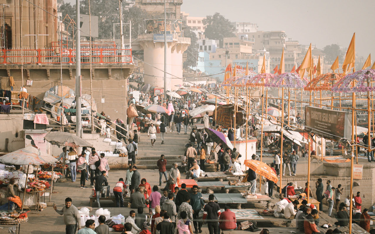 A crowded Varanasi market street near the river with colorful umbrellas