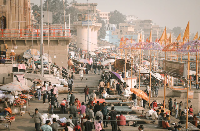 A busy Varanasi market street with colorful umbrellas near the river